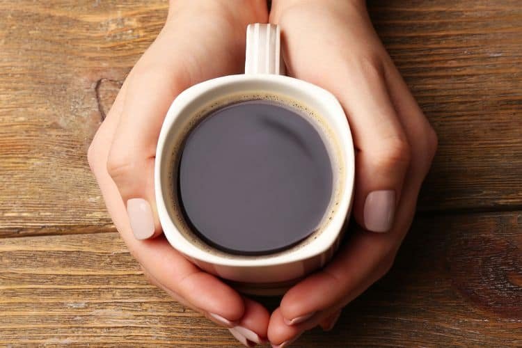 Woman Holding a Cup of Coffee against wooden background